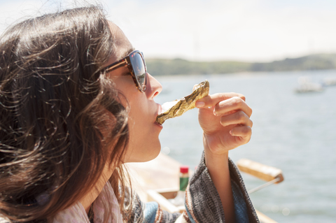 Nahaufnahme einer Frau, die an einem sonnigen Tag im Meer eine Auster isst, lizenzfreies Stockfoto