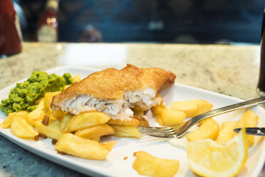 Close-up of fish with French fries and lemon slice in plate on table at restaurant - CAVF16943