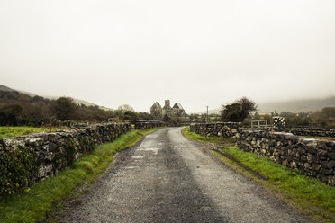 Empty road amidst stone wall against sky during foggy weather - CAVF16944
