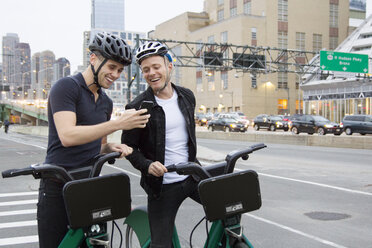 Glückliche Freunde schauen auf ihr Handy, während sie mit Fahrrädern auf der Straße stehen - CAVF16950