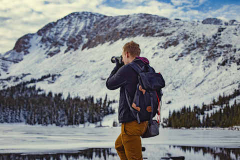 Rückansicht eines fotografierenden Mannes vor einem schneebedeckten Berg, lizenzfreies Stockfoto
