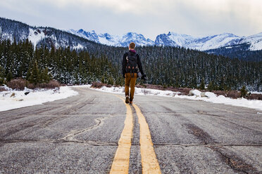 Rückansicht eines Mannes, der auf der Straße gegen schneebedeckte Berge läuft - CAVF16971