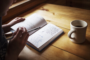 Cropped image of woman writing in book on wooden table - CAVF16975