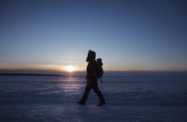 Seitenansicht einer Frau, die auf einem schneebedeckten Feld gegen den Himmel bei Sonnenuntergang läuft - CAVF16986