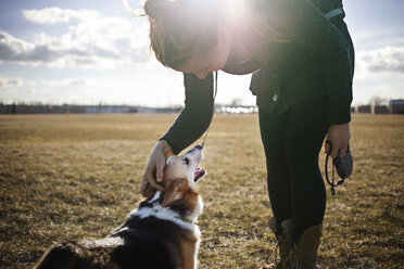 Frau spielt mit Hund auf Feld gegen Himmel an sonnigem Tag - CAVF16988