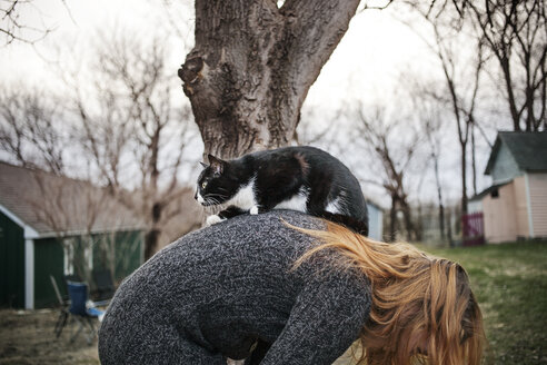 Cat sitting on woman bending at field - CAVF16989