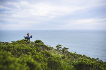 Wanderer beim Fotografieren auf einem Hügel am Meer vor bewölktem Himmel - CAVF17030