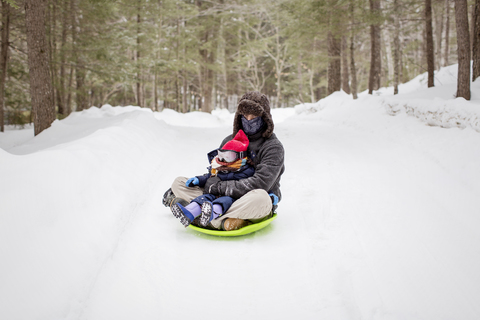 Vater sitzt mit Tochter auf Schlitten auf verschneitem Feld, lizenzfreies Stockfoto