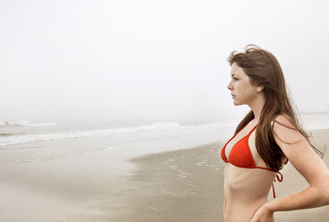 Frau im Bikini-Oberteil schaut weg, während sie auf Sand am Strand gegen den Himmel steht - CAVF17055