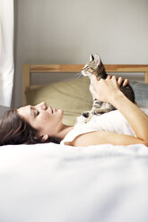 Frau spielt mit Katze, während sie zu Hause auf dem Bett liegt - CAVF17111