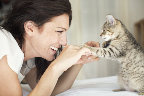 Seitenansicht einer lächelnden Frau, die mit einer Katze auf dem Bett zu Hause spielt - CAVF17116