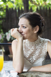 Frau mit Hand am Kinn, die wegschaut, während sie im Restaurant sitzt - CAVF17141