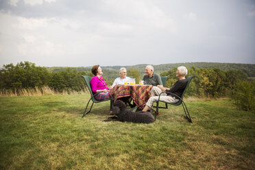 Senior friends sitting at breakfast table in lawn against sky - CAVF17166