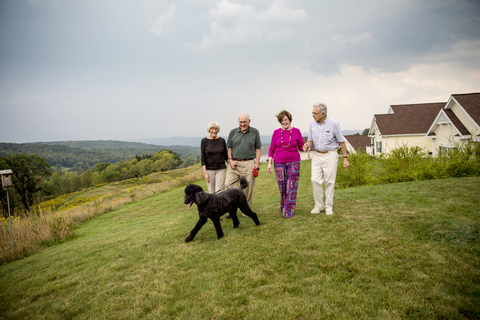 Ältere Paare, die auf einem Feld vor Gebäuden spazieren gehen, lizenzfreies Stockfoto