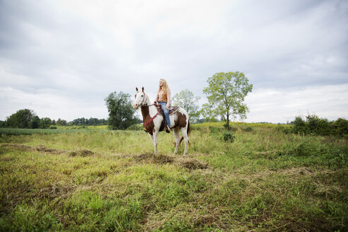 Frau schaut weg, während sie auf einem Pferd gegen den Himmel sitzt - CAVF17204