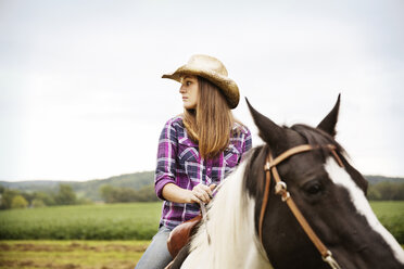 Frau schaut weg, während sie auf einem Pferd im Feld gegen den Himmel sitzt - CAVF17208