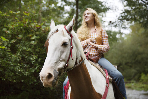 Lächelnde Frau, die beim Reiten auf einem Pferd wegschaut - CAVF17218