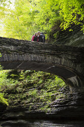 Paar schaut nach unten, während es auf einer Brücke im Wald steht - CAVF17232