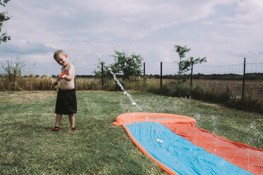 Junge spielt mit Wasserpistole an der Wasserrutsche im Garten - CAVF17242