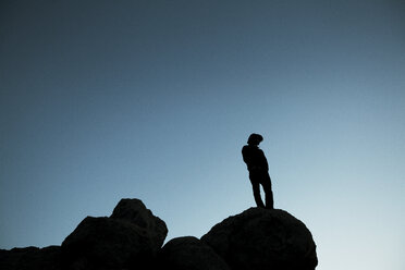 Niedriger Winkel Ansicht der Silhouette Mann auf Felsen gegen klaren blauen Himmel in der Abenddämmerung stehen - CAVF17248