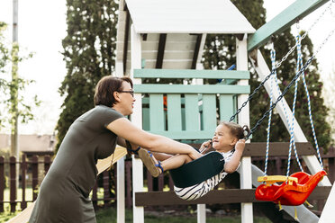 Happy mother pushing daughter sitting on swing in backyard - CAVF17275