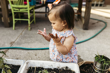 Hoher Winkel Blick auf Baby-Mädchen mit unordentlichen Händen stehen durch Topfpflanzen im Hinterhof - CAVF17281