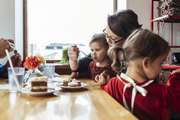 Mutter füttert Mädchen, während die Familie am Restauranttisch sitzt - CAVF17288