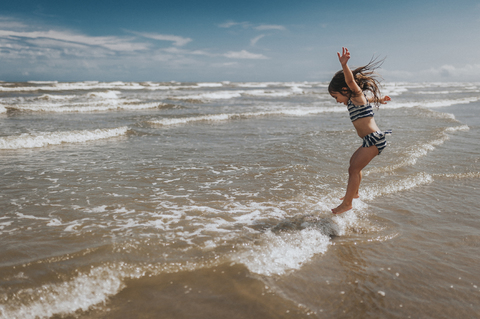 Carefree girl jumping in waves on shore at beach against sky stock photo