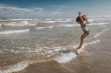 Carefree girl jumping in waves on shore at beach against sky - CAVF17310