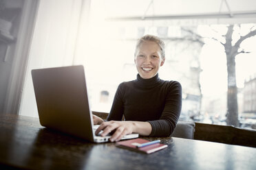 Porträt einer glücklichen jungen Frau mit Laptop am Kaffeetisch - CAVF17314