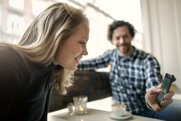 Mann zeigt einer Frau in einem Café sein Smartphone - CAVF17321