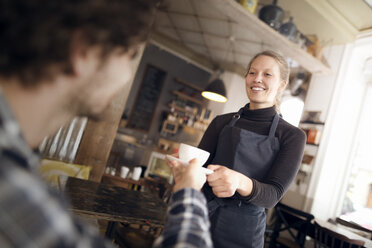 Happy waitress serving coffee to man in cafe - CAVF17324