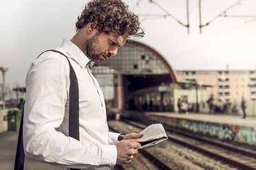 Side view of businessman reading newspaper on railroad station - CAVF17328