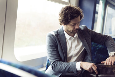 Businessman searching in bag while sitting in train - CAVF17332