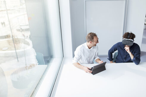 Engineer looking at male colleague examining virtual reality simulator in office - CAVF17376