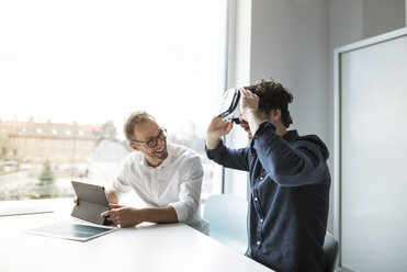 Smiling engineer looking at colleague examining virtual reality simulator in office - CAVF17377