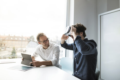 Ein lächelnder Ingenieur betrachtet einen Kollegen, der einen Virtual-Reality-Simulator im Büro untersucht - CAVF17377