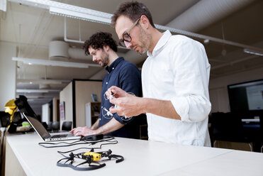 Techniker, der eine Drohne untersucht, während ein Kollege einen Laptop am Tisch im Büro benutzt - CAVF17382