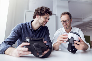 Techniker untersuchen Virtual-Reality-Simulatoren, während sie an einem Tisch im Büro sitzen - CAVF17390