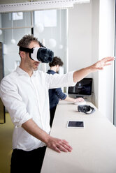 Businessman examining virtual reality simulator while coworker using computer in office - CAVF17394