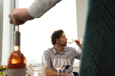 Abgeschnittene Hand eines Barkeepers, der eine Flasche hält, während ein Kunde im Hintergrund Wein probiert - CAVF17403