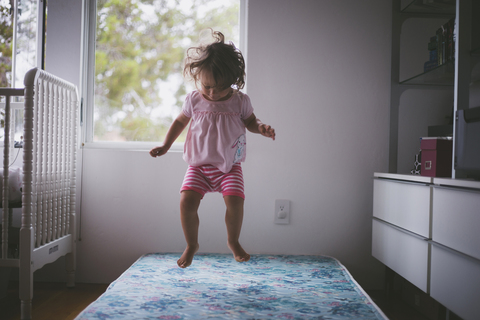 Fröhliches Mädchen springt zu Hause auf dem Bett herum, lizenzfreies Stockfoto