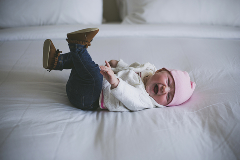 Fröhliches Baby, das lachend auf dem Bett zu Hause liegt, lizenzfreies Stockfoto