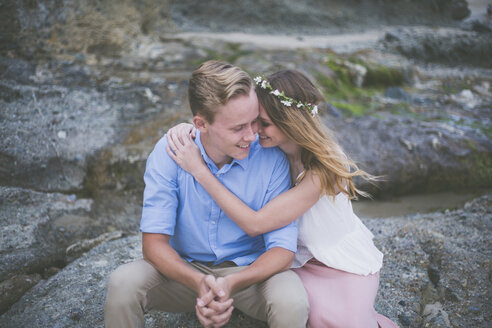 Glückliches Paar sitzt auf einem Felsen am Strand - CAVF17447