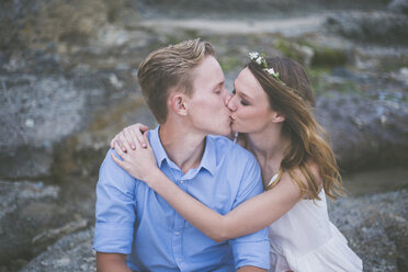 Paar küsst sich auf einem Felsen am Strand sitzend - CAVF17448