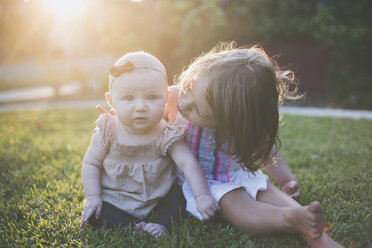 Portrait of baby girl sitting with sister on grassy field at backyard - CAVF17460