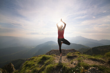 Frau übt Yoga, während sie auf einem Berg gegen den Himmel steht - CAVF17463