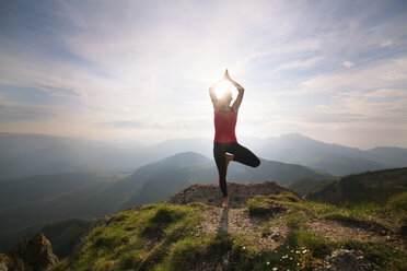 Woman practicing yoga while standing on mountain against sky - CAVF17463