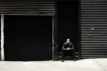 Nachdenklicher Mann sitzt auf Stufen vor einer schwarzen Wand - CAVF17534