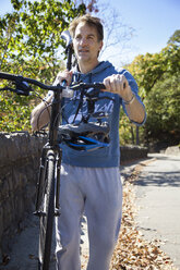 Mann trägt Fahrrad auf der Schulter, während er auf der Straße geht - CAVF17606
